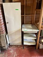 Metal storage cabinet and metal table placed side by side in a basement environment with concrete floor and wooden walls.