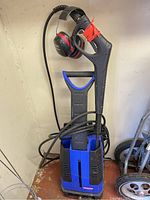 Front view of Simoniz S1700 pressure washer with hose, spray gun, and ear protection earmuffs hanging on gun handle.