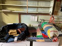 Photo showing both the black rolling luggage bag with attached pouches and the colorful patchwork quilt rolled and laid out over a washing machine.