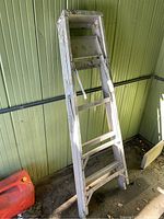 Photo of aluminum 5 foot step ladder leaning against green wall, showing full ladder