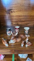 Photo of three Royal Doulton Toby mugs and multiple ceramic rabbits arranged on a wooden shelf.