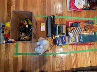 Overall lot with boxes containing toys, games, microscope, and toy cars spread on hardwood floor
