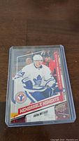Photo showing Auston Matthews rookie card featuring action shot in Toronto Maple Leafs uniform inside clear plastic protective case on wooden surface.