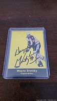 Front view of the Wayne Gretzky autographed hockey card showing his image in a skating pose, yellow background, and autograph prominently displayed.