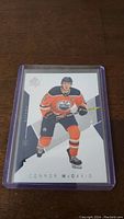 Front view of a Connor McDavid Upper Deck hockey trading card in protective plastic case on a wooden surface.