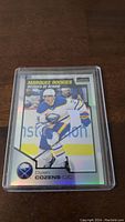 Front view of Dylan Cozens rookie hockey card in plastic sleeve, showing player in Buffalo Sabres uniform and Marquee Rookies branding.