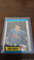 Photo showing Joe Sakic rookie hockey card in a hard plastic protective case, front view.