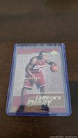 Photo of a LeBron James rookie basketball card in a protective plastic case showing front design with LeBron in Cavaliers uniform and 'LeBron's Diary' text.