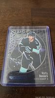 Hockey card of Matty Beniers in Seattle Kraken uniform with holographic design inside a protective plastic holder.