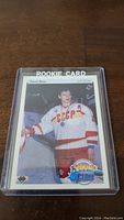 Photo shows Pavel Bure rookie hockey card in clear protective plastic case on wood surface.