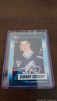 Photo of a Sidney Crosby rookie hockey card protected in a plastic sleeve showing the front of the card with a young Sidney Crosby in hockey uniform.