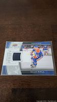 Front view of Taylor Hall Upper Deck hockey card with embedded blue fabric jersey piece and player photo in Oilers uniform.