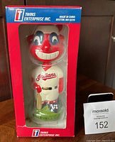 Front view of the Cleveland Indians bobblehead doll in original red box with clear window showing the figure, the doll has red face paint and blue eye markings, holds a bat, and has 'Indians' on jersey.