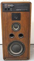 Front view of Koss CM 1020 single speaker showing wood veneer cabinet, tuning meter, control knobs, tweeter, mid-range driver, woofer, and dual ports.