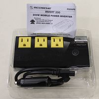 Black Scosche invert 200 power inverter with 3 yellow AC outlets, power and protect indicators, power button, and included cigarette lighter plug cable, displayed inside clear plastic packaging.