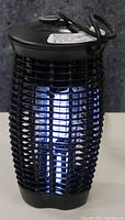 Front view of black electric insect killer illuminated with blue ultraviolet light on a white surface.