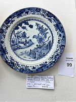 Front view of 18th century antique round porcelain plate featuring blue pagoda and landscape design, with gilt rim and some visible age wear and crazing.