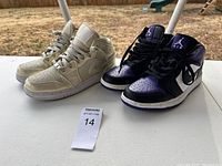 Both pairs of Nike Air Jordan 1 sneakers displayed side by side on a white table outdoors, showing condition and size.