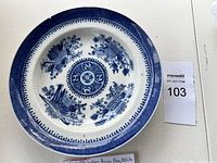 Top-down close-up photo of the 19th century antique Asian blue and white porcelain bowl showing central circular motif, chrysanthemum flowers, bamboo, and decorative rim.