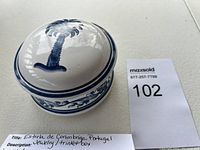 White ceramic circular jewelry/trinket box with blue hand-painted floral and vine designs and matching lid with a flower motif on top.