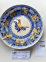 Full view of the round antique plate with central yellow bird and blue, green, yellow painted leaf patterns around the rim.