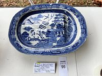 Top view of the antique blue and white ceramic platter with willow pattern showing pagodas, trees, bridges, and water scene.
