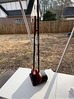 Full view of broom and dustpan with long black handles on a white table outdoors