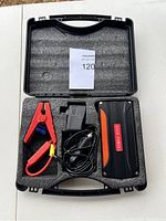Car jump starter kit components in foam cutout inside black carrying case.