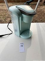 Side view of light blue Keurig coffee maker showing water reservoir, power cord, and drip tray.