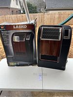 Photo of the Lasko ceramic heater next to its original box showing the heater's front and wood grain finish.