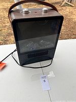 Front view of the faux wood finished space heater showing glass/plastic front panel and ventilation grille below.