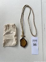 Full view of necklace with hexagonal pendant and branded cloth pouch beside it