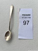 Small sterling silver baby spoon shown next to lot number card for scale.