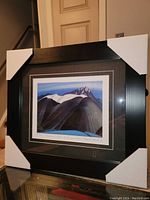 Framed fine art print by Lawren Harris titled 'Mountains East of Maligne Lake' with black wide frame and protective corners, showing the mountain landscape with snow caps.