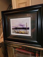 Black framed print showing colorful lake and canoe scene by Tom Thomson, title and edition number visible