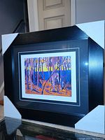 Framed fine art print in black frame with white and black double matting, showing vibrant forest scene with purple and orange tones.