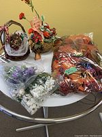 Table displaying various vintage artificial flowers and arrangements including baskets and bags of leaves