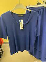 Blue short sleeve top with scoop neckline and decorative knot, tagged new, on light-colored hanger