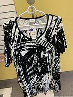 Photo of a black and white abstract pattern ladies top with short sleeves on a hanger and wall background