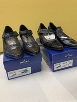Two pairs of brand new black ladies shoes on their blue Artika boxes, size 38, both with pointed toes and ankle straps, one with snakeskin texture