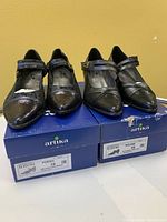 Two pairs of black ladies shoes by Arutka, size 39, on top of their respective boxes