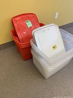 Four red plastic storage bins stacked with lids leaning inside and four translucent white plastic storage bins stacked with lids on top.