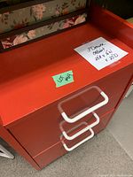 Front view of the small red drawer unit showing the three white-handled drawers and top surface with raised edges