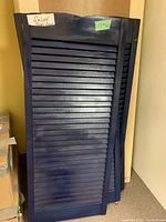 Two pairs of vintage wooden saloon swinging doors painted blue stacked against wall, showing their slatted design and curved upper edges.