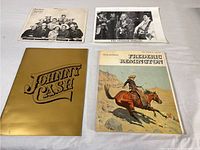 Four books laid on white surface including Johnny Cash gold cover book and Frederic Remington book