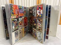 Opened binder showing collectible cards in plastic sleeves, featuring Disney characters and other comics.