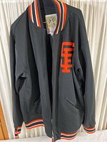 Full view of black long sleeve jacket with orange and white striped collar, cuffs, and hem, with a zipper front.