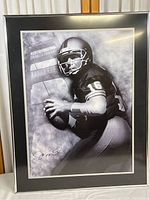 Framed Joe Montana poster showing him in football gear with football, unauthenticated signature visible.