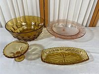 Four colored glass dishes on white cloth, amber and pink hues, varying sizes and shapes