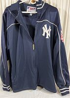 Front view of navy blue jacket with zip-up front and New York Yankees logo on chest, showing ribbed cuffs and waistband with white stripes.